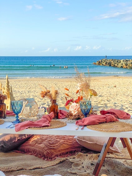 A beach setting with a table set for a meal, decorated with flowers and a sand sculpture. 1