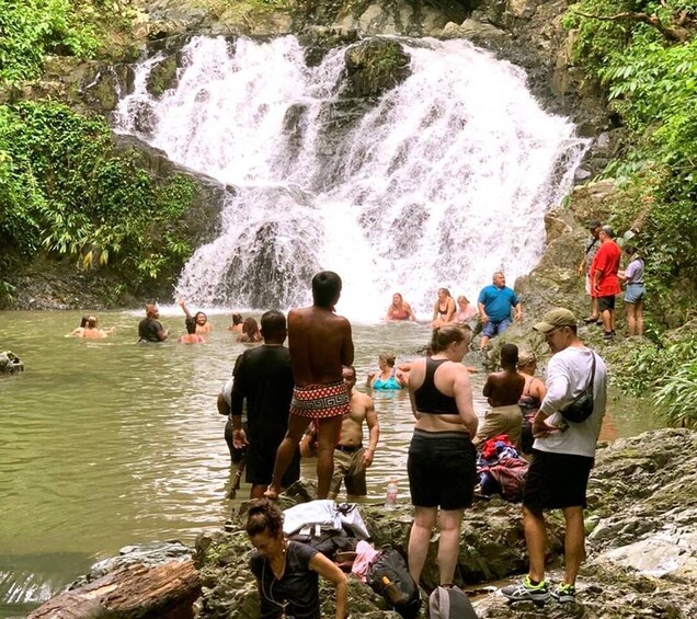 Ein Wasserfall mit badenden und stehenden Personen in einer natürlichen Umgebung. 4