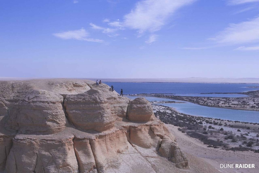 A rocky desert landscape with a clear blue sky and a distant body of water. 4