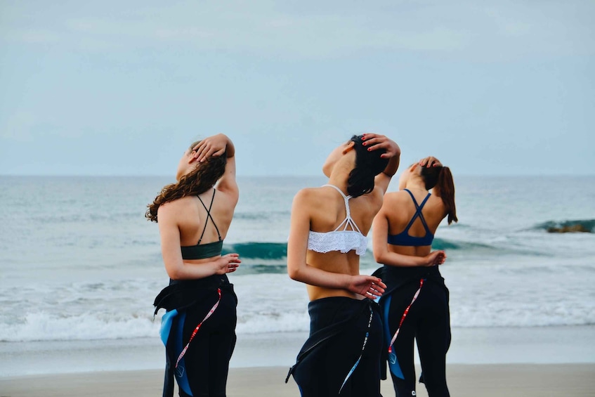 Three people standing on a beach with the ocean in the background. 4
