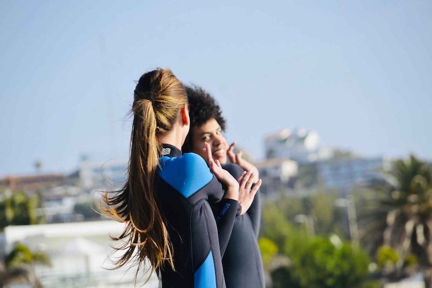 Two people embracing, one with a ponytail, in an urban setting with buildings and greenery in the background. 1