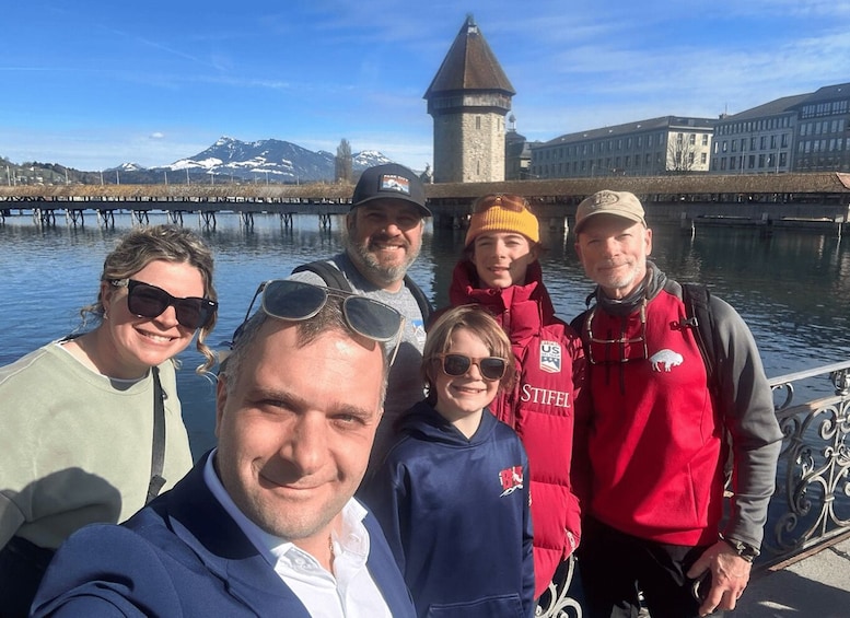 A group of people standing by a body of water with a tower and buildings in the background. 3