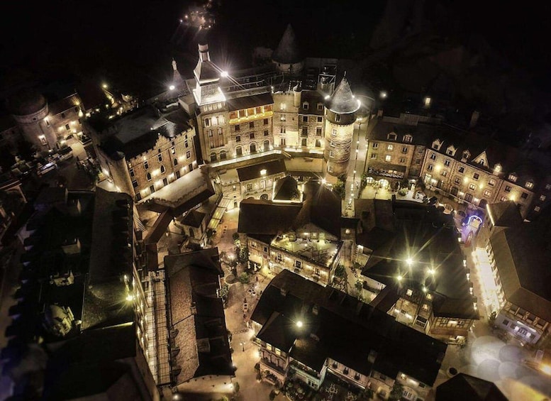 An aerial view of a historic town square at night, featuring a prominent castle-like building with multiple towers and a central courtyard. 3