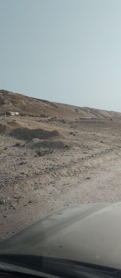 A desert landscape with sparse vegetation, a road, and a few tents in the distance. 4