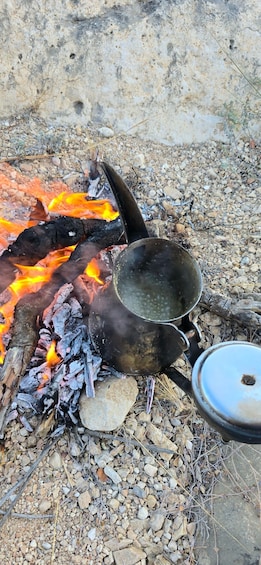 A campfire with cooking pots and a pan on a rocky ground. 3