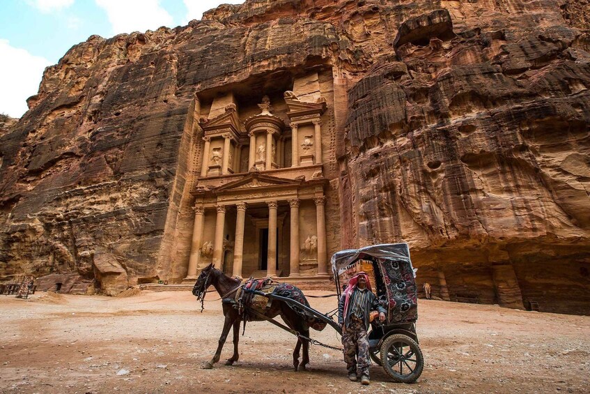 A carved rock facade with columns and a horse-drawn carriage in front. 1