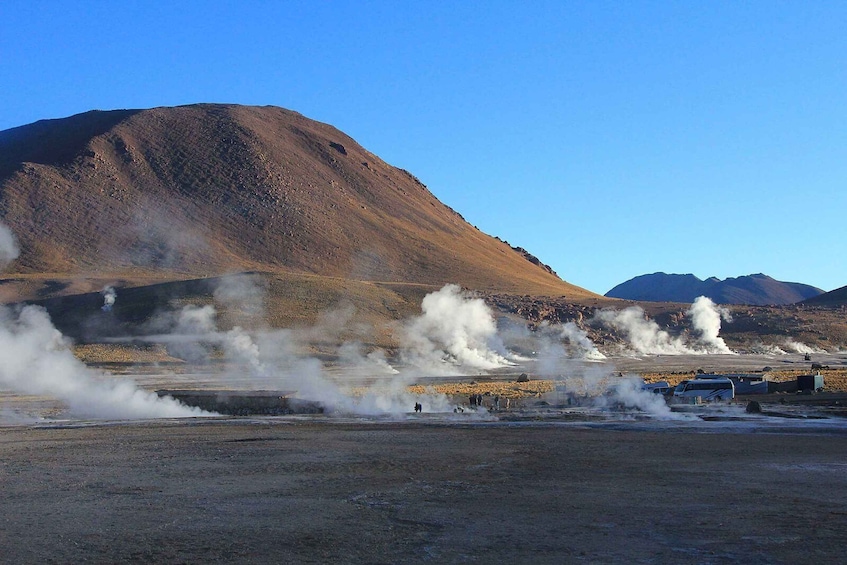 A geothermal area with steam vents and a distant mountain. 4