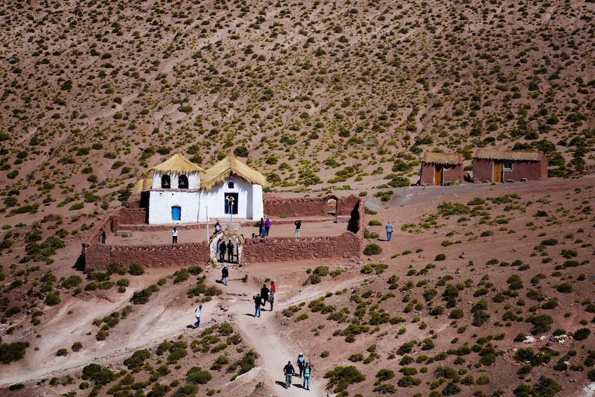 A white building with a thatched roof surrounded by a small community in a desert landscape. 5