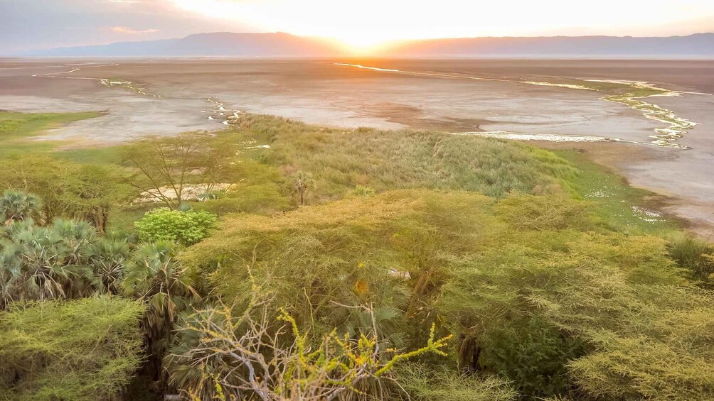 A landscape with a river, vegetation, and distant mountains during sunset. 2