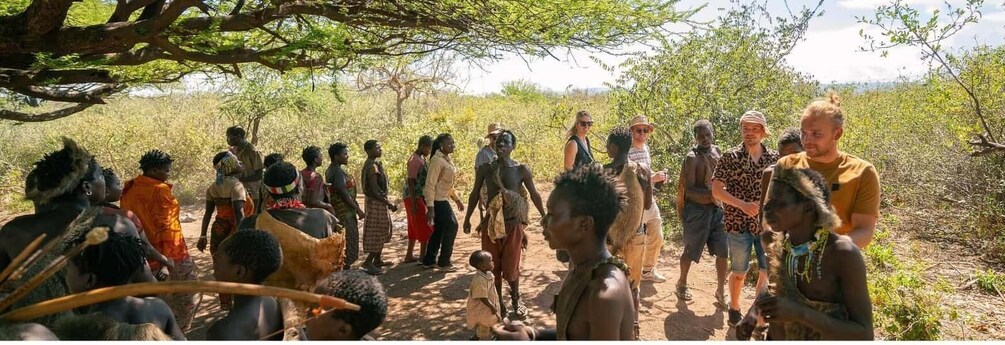 A group of people standing outdoors, some wearing traditional attire, with a camel in the foreground. 1