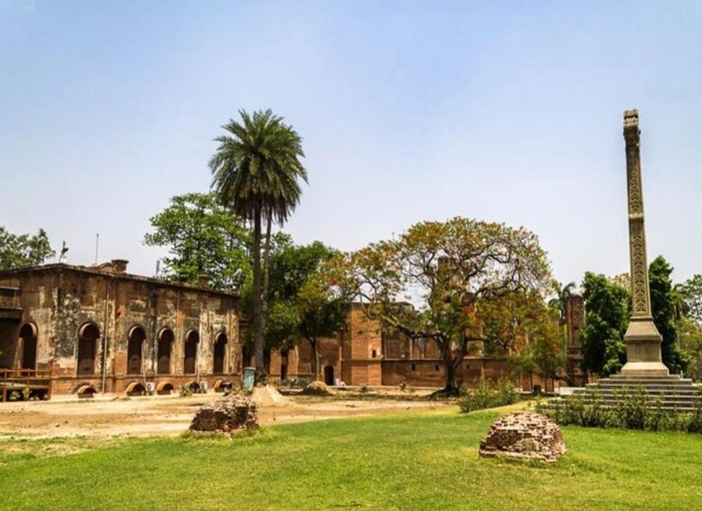 An ancient building with arched doorways, a palm tree, and a tall obelisk in a grassy area. 5