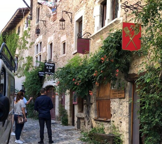 A narrow cobblestone street lined with old stone buildings, some with ivy and flowers. There are signs hanging from the buildings, including one that says "Orenier à Sel." 2