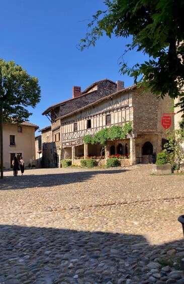 A cobblestone street with a traditional stone building featuring a timber-framed facade and a sign for a local wine shop. 1