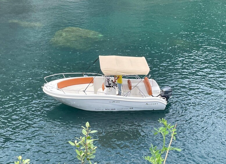 En lille hvid motorbåd med orange interiør og et beige tag på roligt vand. 1