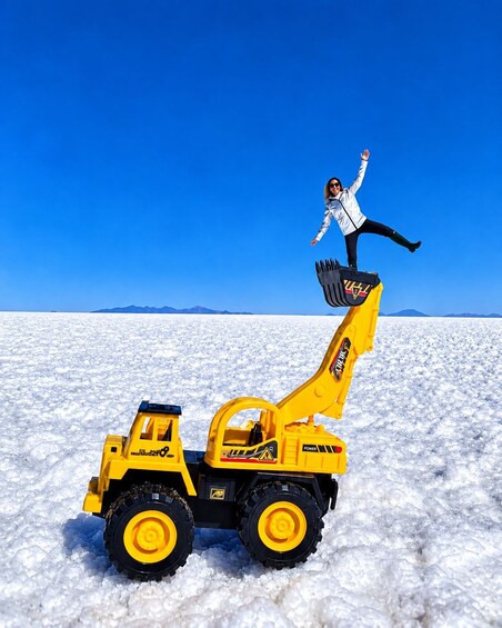 A person standing on a toy excavator in a snowy landscape with mountains in the background. 3