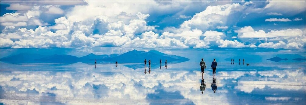 A reflective lake with people walking, mountains in the background, and a cloudy sky. 5