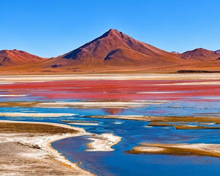 A salt flat with colorful mineral deposits and a mountain in the background. 2