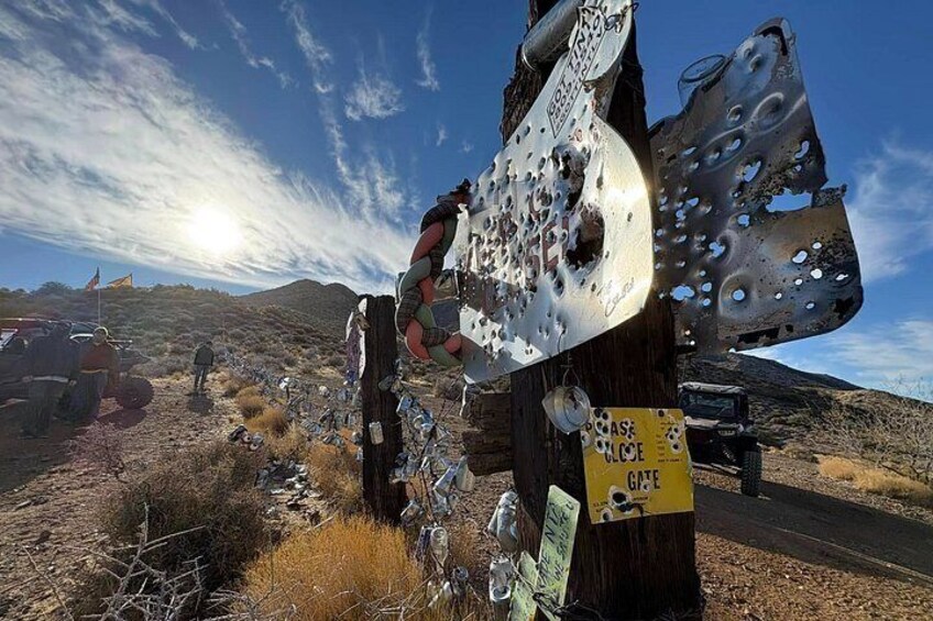 A desert landscape with a metal structure covered in bullet holes, a sign reading 'CLOSE CALL,' and a vehicle in the background. 5