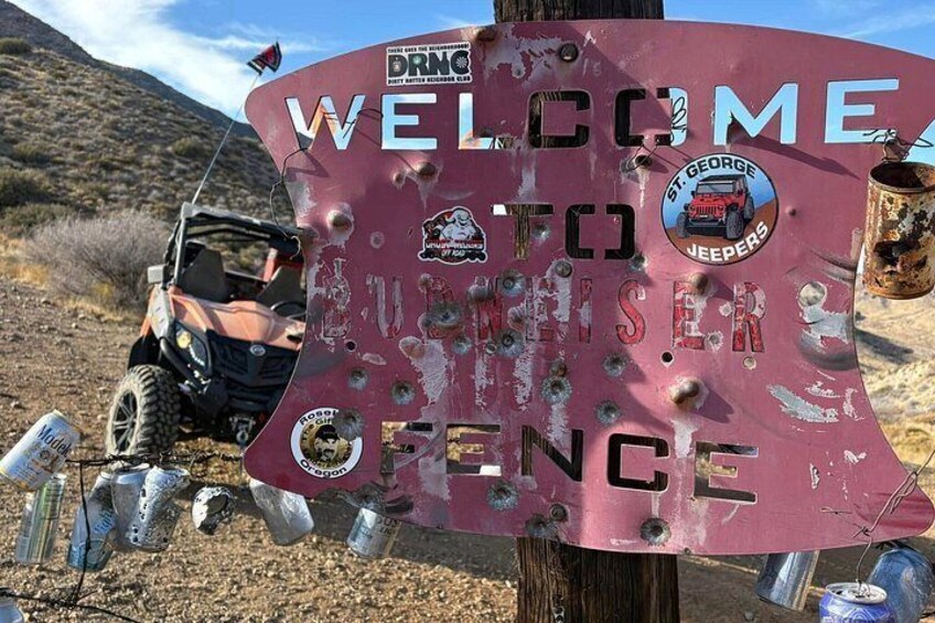 A rusted welcome sign with stickers, a Jeep, and a desert landscape. 4