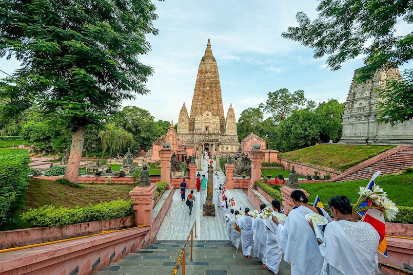 A temple complex with a central stupa, surrounded by lush greenery and a group of people in white robes ascending the steps. 5