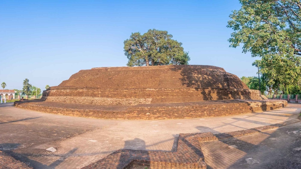 A large, ancient brick structure with a flat top and a circular base, surrounded by trees and a clear sky. 4