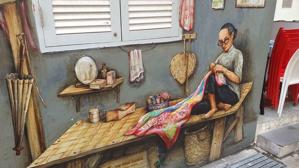 A mural of a man sitting on a wooden bench, sewing a colorful fabric. 2