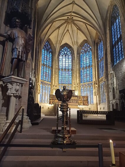 A cathedral interior with stained glass windows, a large statue, and a central altar. 1