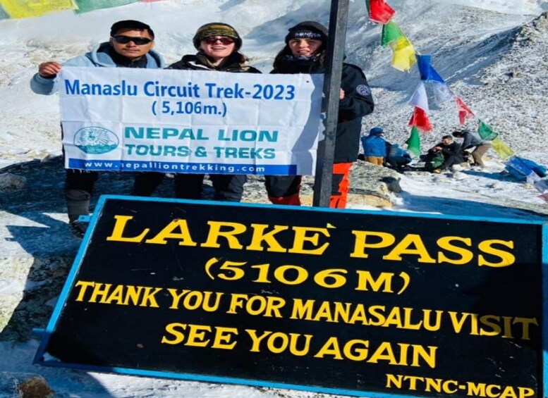 A group of people holding a banner for the Manaslu Circuit Trek-2023, with a sign for Larke Pass (5106m) below. 2