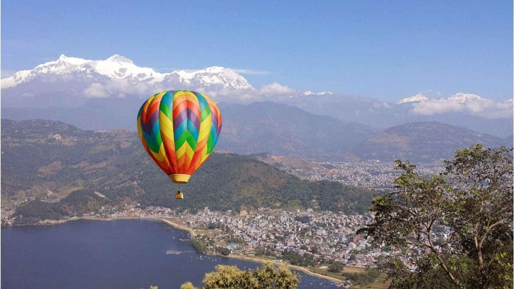 A colorful hot air balloon flying over a coastal city with mountains in the background. 2
