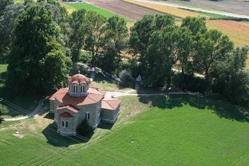 Una iglesia con techo rojo rodeada de campos verdes y árboles. 2