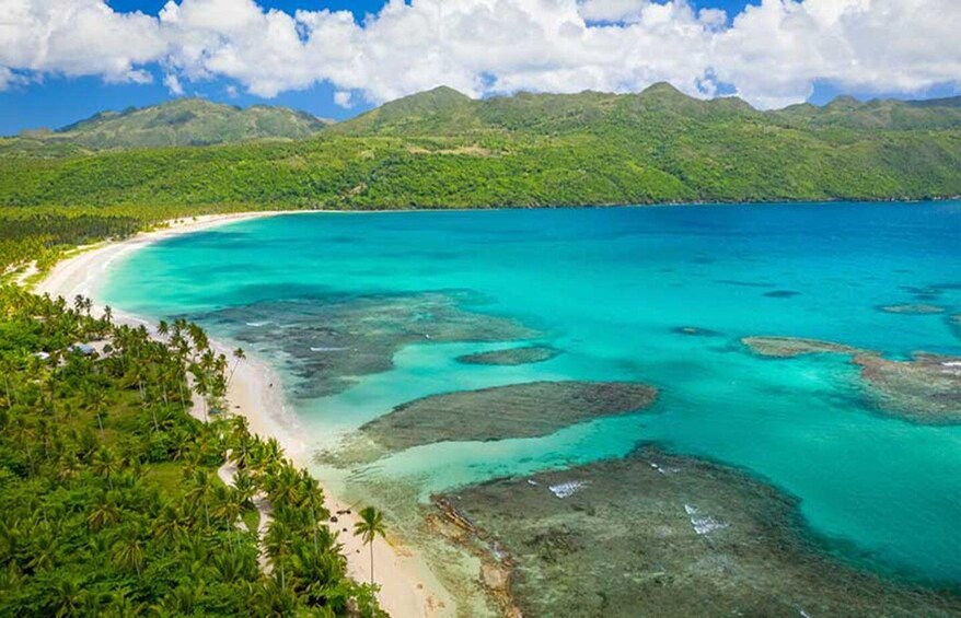 Una playa tropical con aguas turquesas cristalinas, una orilla arenosa y colinas verdes exuberantes al fondo. 5