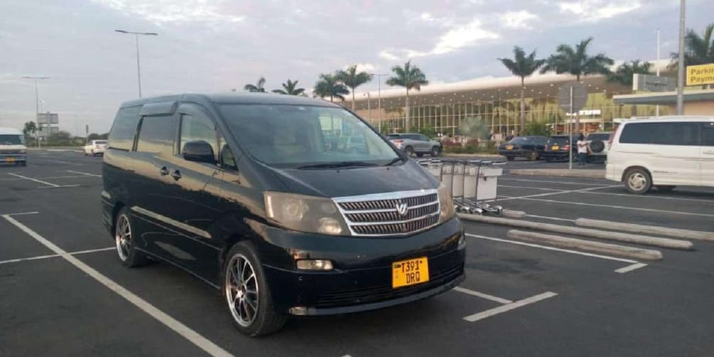 A black van parked in a lot with palm trees and a building in the background. 1