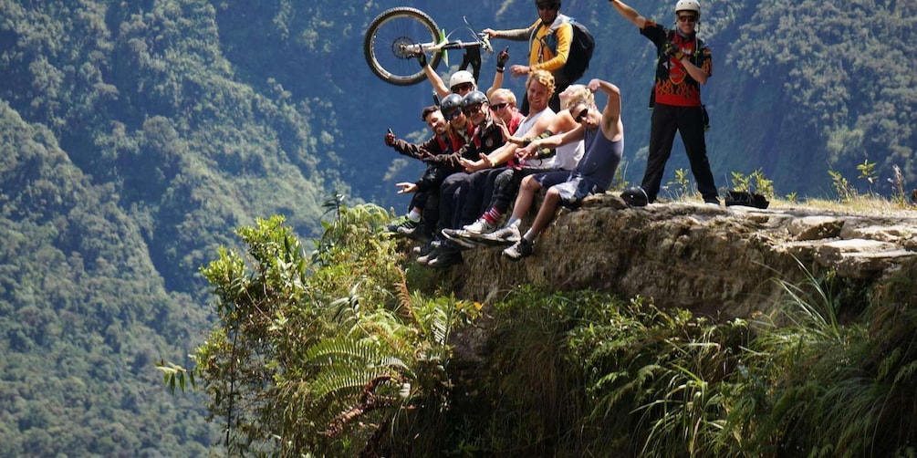 A group of people sitting on a cliff edge with a mountainous landscape in the background. 2