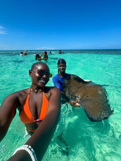 Two people in clear turquoise water, one holding a stingray. 1