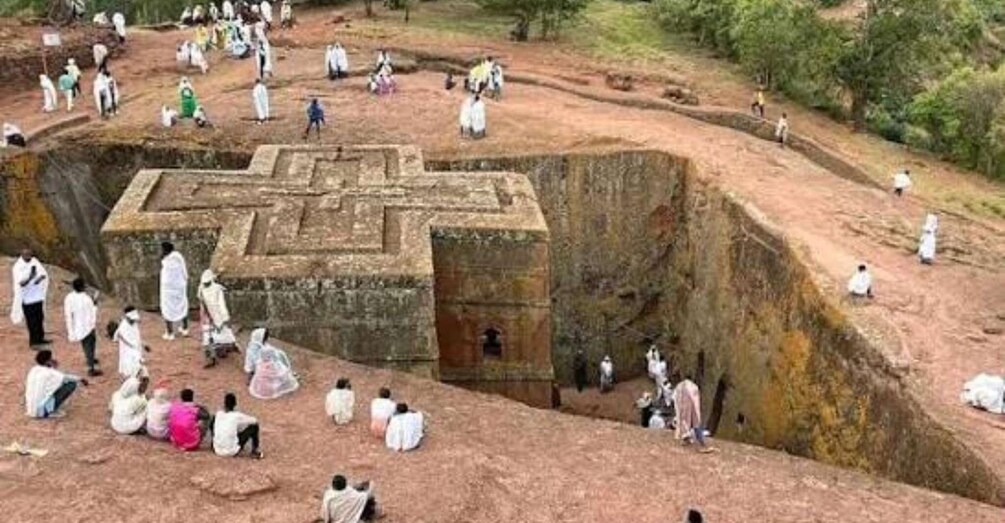 A large cross-shaped stone structure surrounded by people. 3