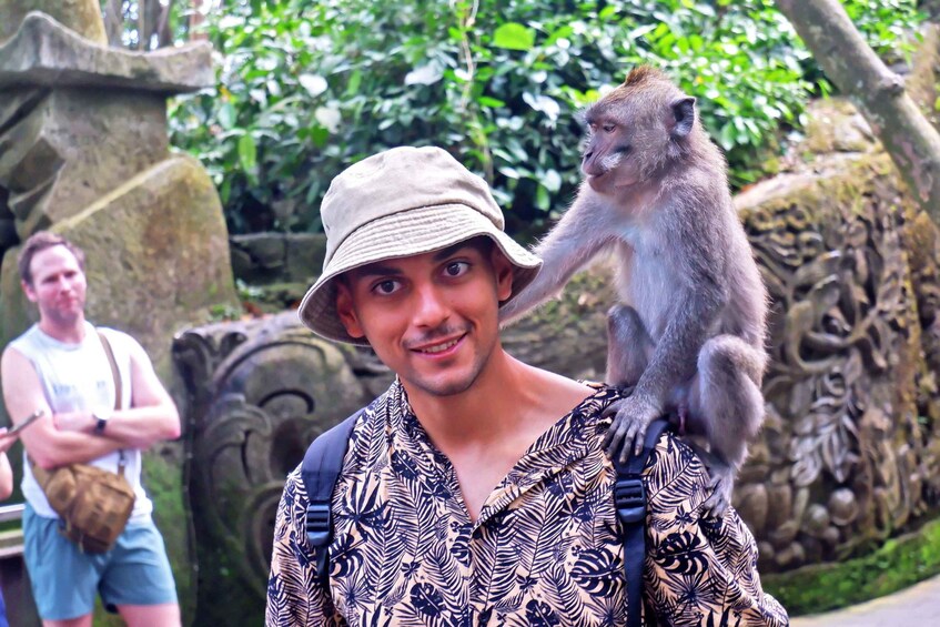 A person with a monkey on their shoulder, surrounded by stone carvings and greenery. 5
