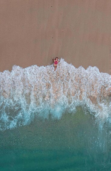 A person in a pink swimsuit on a sandy beach with waves crashing onto the shore. 1