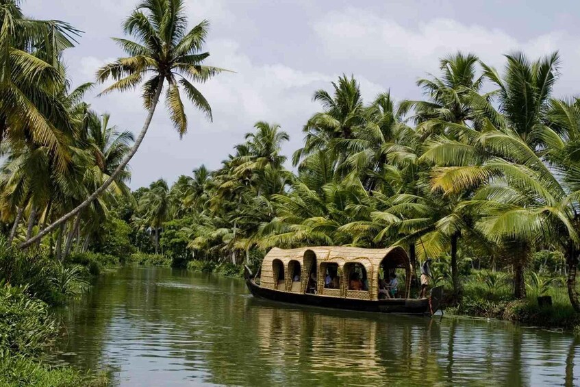 A traditional boat with a thatched roof navigating a river surrounded by palm trees. 1