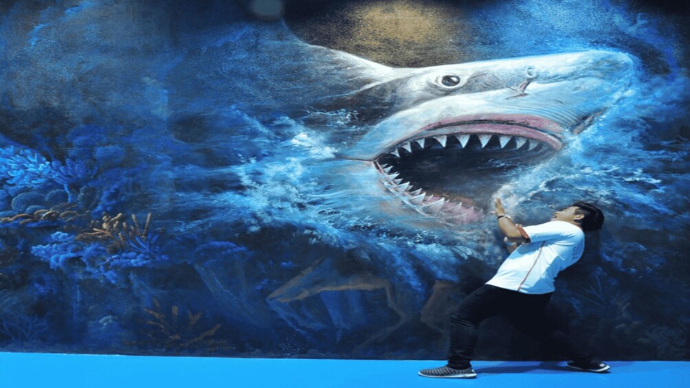 A man in a white shirt and black pants standing in front of a mural of a shark. 2