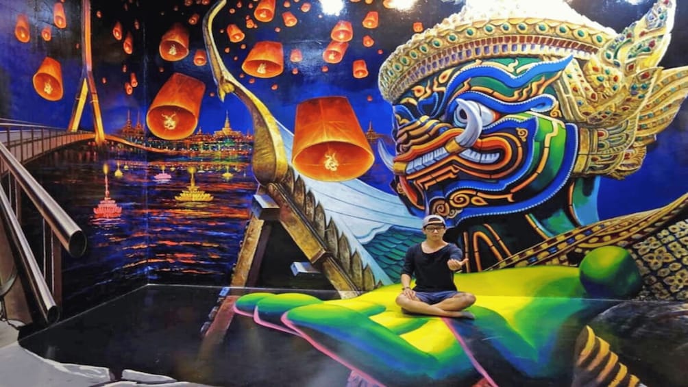 A person sitting on a colorful, illuminated platform with a mural of a dragon and floating lanterns in the background. 3