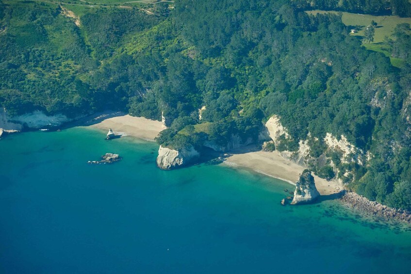 An aerial view of a coastal area with a sandy beach, clear turquoise waters, and dense green forested hills. 1