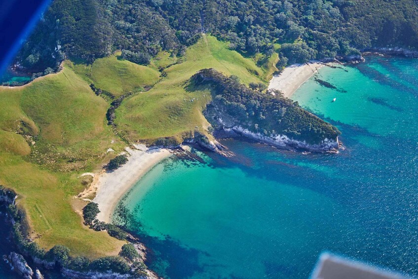 An aerial view of a coastal landscape with green hills, turquoise waters, and a sandy beach. 2