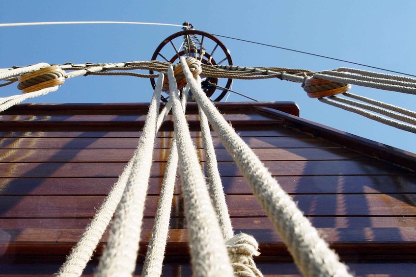 A close-up of a ship's rigging with multiple ropes and a wheel. 5