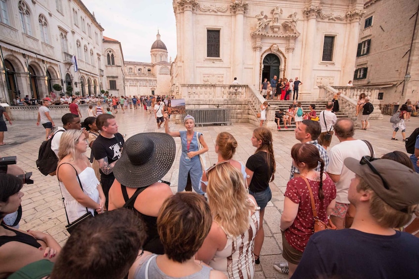 A group of tourists gathered in a historic square with ornate buildings and a fountain. 2