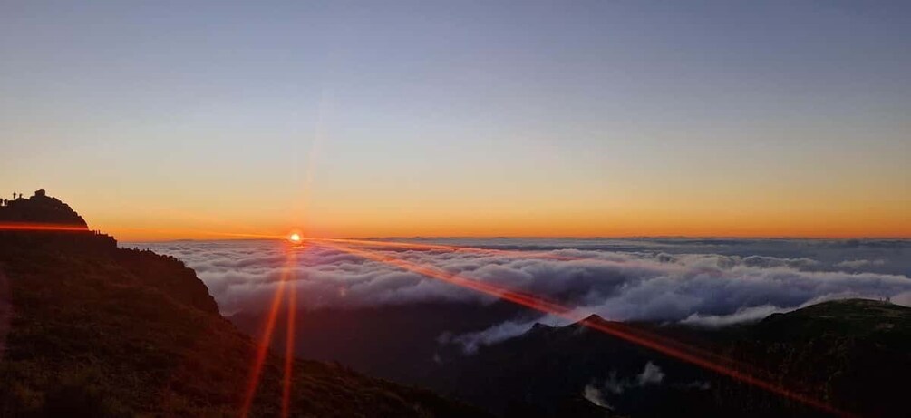 A sunrise over a mountainous landscape with clouds below. 1