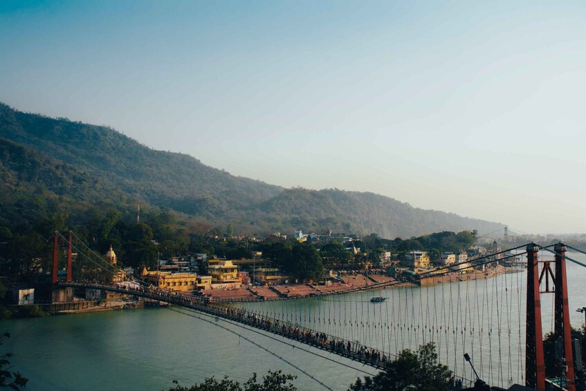 A suspension bridge over a river with a town and hills in the background. 2