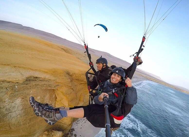 A person paragliding over a coastal area with a clear sky and a distant paragliding canopy. 4