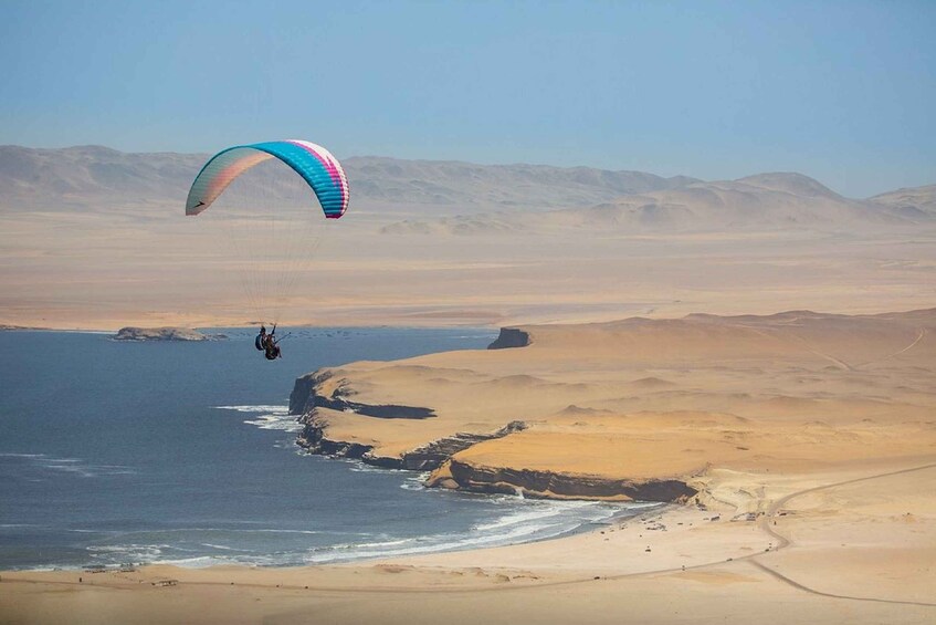 A person paragliding over a desert landscape with a body of water and mountains in the background. 5