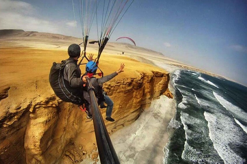 A person paragliding over a cliff with a vast desert and ocean below. 2