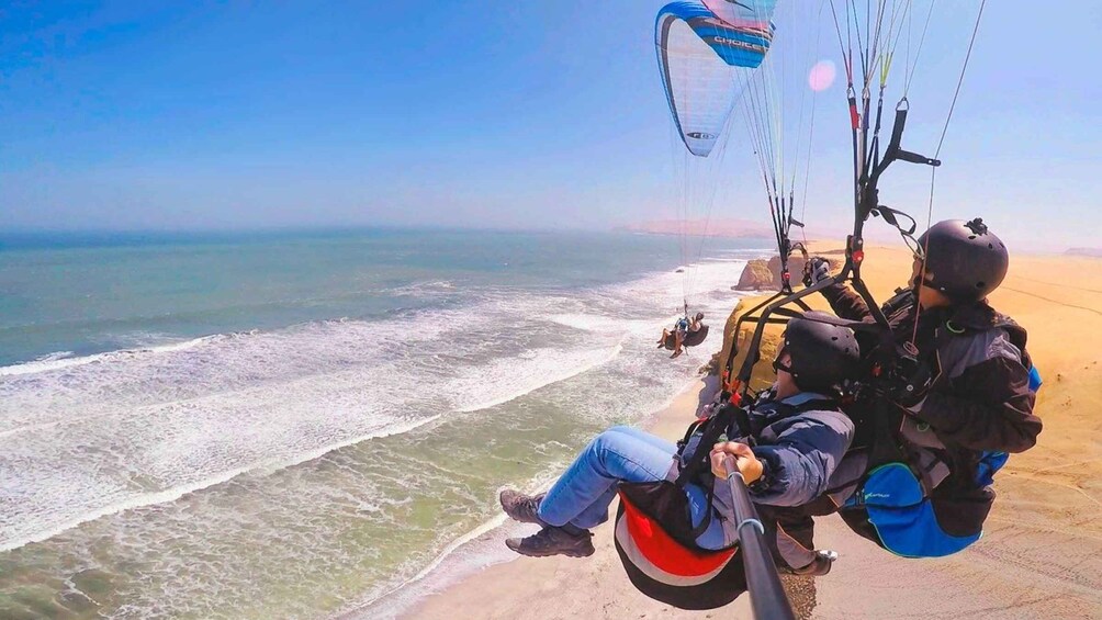 A person parasailing over a beach with waves crashing onto the shore. 1